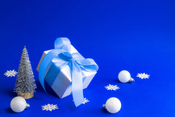 Winter background blue. White gift box with blue ribbon, winter tree, Snowflakes and Silver balls in Christmas composition on blue background for greeting card. Xmas, winter, new year concept.