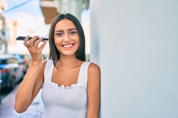 Young latin girl smiling happy talking on the smartphone leaning on the wall.