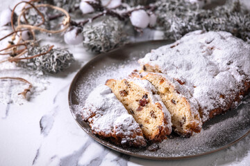 Traditional homemade german Christmas baking stollen cake bread on plate with silver xmas decorations over white marble background.