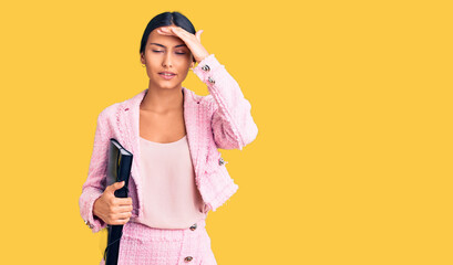 Young beautiful latin girl wearing business clothes holding binder stressed and frustrated with hand on head, surprised and angry face