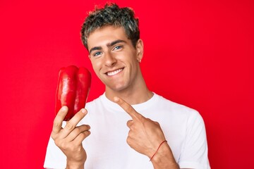 Young handsome man holding red pepper smiling happy pointing with hand and finger