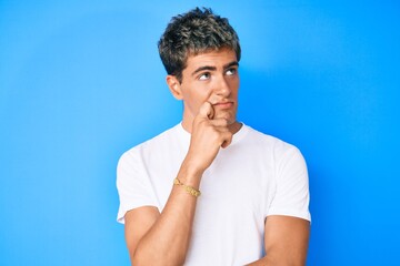 Young handsome man wearing casual white t shirt serious face thinking about question with hand on chin, thoughtful about confusing idea