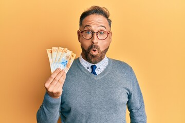 Handsome middle age man holding swiss franc banknotes scared and amazed with open mouth for surprise, disbelief face