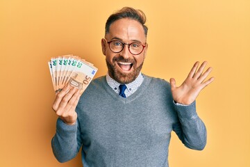 Handsome middle age man holding bunch of 50 euro banknotes celebrating achievement with happy smile...