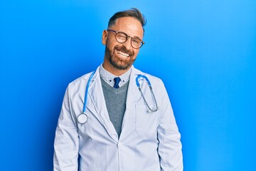 Handsome middle age man wearing doctor uniform and stethoscope winking looking at the camera with sexy expression, cheerful and happy face.