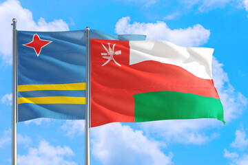 Fototapeta na wymiar Oman and Aruba national flag waving in the windy deep blue sky. Diplomacy and international relations concept.