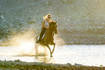 A girl rides a horse in the evening in the water along the river bank