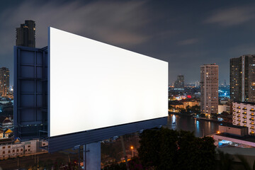 Blank white road billboard with Bangkok cityscape background at night time. Street advertising poster, mock up, 3D rendering. Side view. The concept of marketing communication to sell idea.