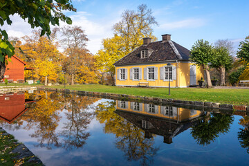 Fototapeta na wymiar Small cozy old house of the past centuries with 4 windows and a tiled roof. A yellow house in the countryside is reflected in the water on a sunny autumn day. Country villa cottage in vintage style.