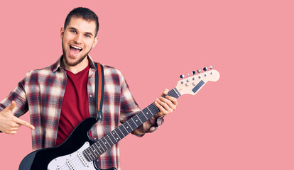 Young handsome man playing electric guitar smiling happy pointing with hand and finger