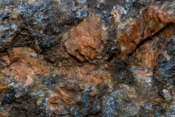 A close-up of a granite cobblestone with small inclusions of quartz under high magnification. Background with red granite in soft focus.