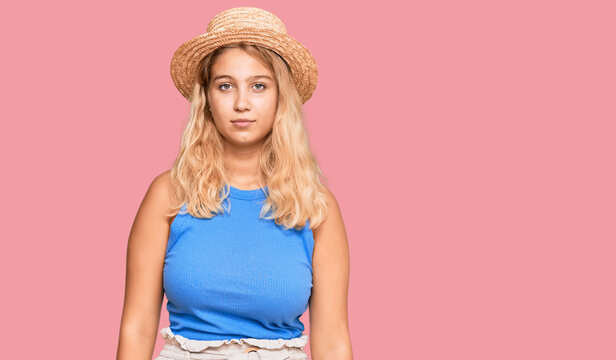 Young blonde girl wearing summer hat with serious expression on face. simple and natural looking at the camera.