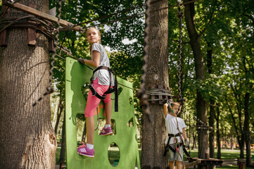 Obraz na płótnie Canvas Girl and boy in equipment climbs in rope park