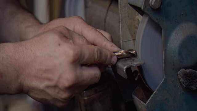 Locksmith sharpens a drill on emery in the workshop