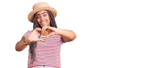 Young african american woman with braids wearing summer hat smiling in love doing heart symbol shape with hands. romantic concept.