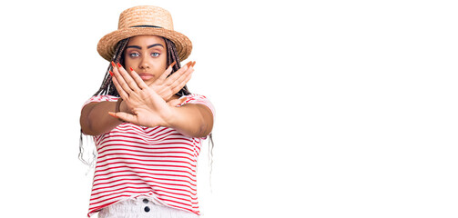 Obraz na płótnie Canvas Young african american woman with braids wearing summer hat rejection expression crossing arms doing negative sign, angry face