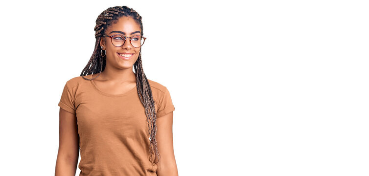Young african american woman with braids wearing casual clothes and glasses looking away to side with smile on face, natural expression. laughing confident.