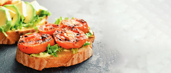 Bruschetta with tomatoes and mozzarella. on a dark background. Bruschetta with avocado and feta. Appetizing sandwiches with grilled tomatoes. Italian snack. Vegetarian wholesome food. Copy space