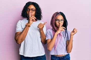 Beautiful african american mother and daughter wearing casual clothes and glasses asking to be quiet with finger on lips pointing with hand to the side. silence and secret concept.