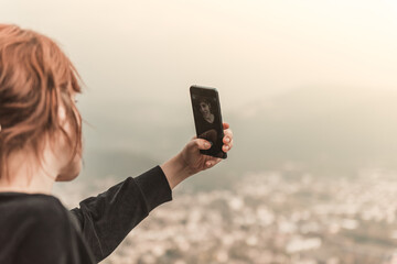 The red-haired girl taking photo with smart phone at the mountain peak