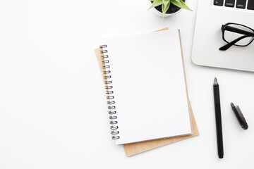 Blank notebook with pen are on top of white office desk table with laptop computer and supplies. Top view with copy space, flat lay.