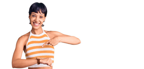 Young brunette woman with short hair wearing casual clothes in hurry pointing to watch time,...