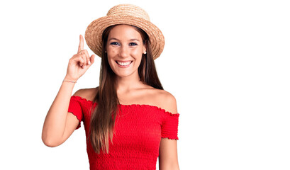 Young beautiful hispanic woman wearing summer hat pointing finger up with successful idea. exited and happy. number one.