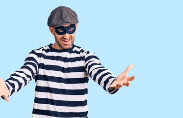 Young handsome man wearing burglar mask looking at the camera smiling with open arms for hug. cheerful expression embracing happiness.