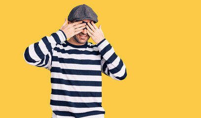 Young handsome man wearing burglar mask covering eyes with hands smiling cheerful and funny. blind concept.