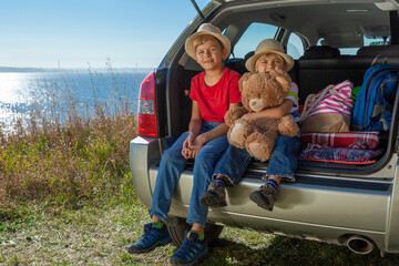 Family vacation by the sea. Two boys are sitting in the trunk of a car. The tailgate is open up....