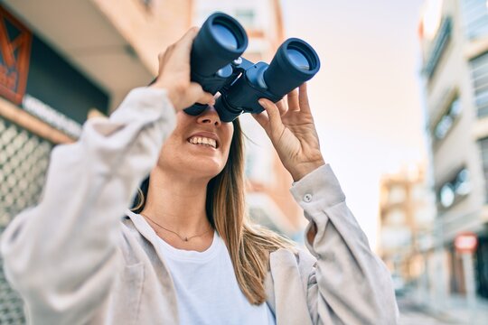 Young caucasian woman smiling happy looking for new opportunity using binoculars walking at the city.