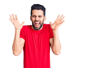 Fototapeta premium Young handsome man with beard wearing casual t-shirt celebrating mad and crazy for success with arms raised and closed eyes screaming excited. winner concept