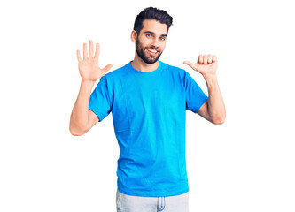 Young handsome man with beard wearing casual t-shirt showing and pointing up with fingers number six while smiling confident and happy.