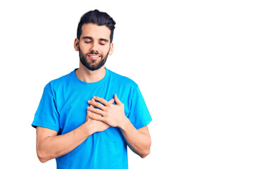 Young handsome man with beard wearing casual t-shirt smiling with hands on chest with closed eyes and grateful gesture on face. health concept.