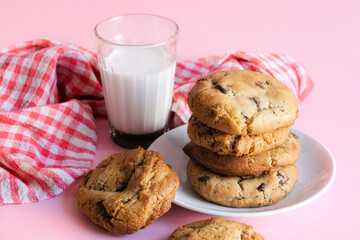 Stack of chocolate chip cookies beside a glass of milk in front of a pink background