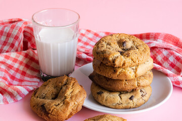 Stack of chocolate chip cookies beside a glass of milk in front of a pink background