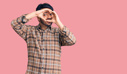 Young hispanic man wearing casual clothes doing heart shape with hand and fingers smiling looking through sign