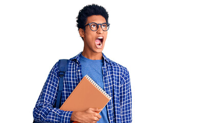 Young african american man wearing student backpack holding book angry and mad screaming frustrated and furious, shouting with anger. rage and aggressive concept.