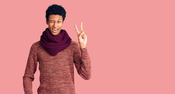 Young african american man wearing casual winter sweater and scarf smiling with happy face winking at the camera doing victory sign with fingers. number two.