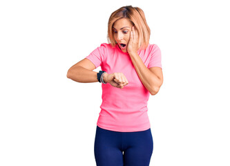 Young blonde woman wearing sportswear looking at the watch time worried, afraid of getting late