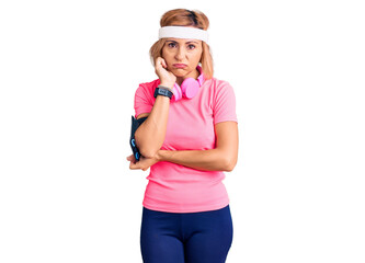 Young blonde woman wearing sportswear and headphones thinking looking tired and bored with depression problems with crossed arms.