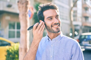 Young hispanic man smiling happy listening audio message using smartphone at city.