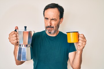Middle age hispanic man holding italian coffee maker skeptic and nervous, frowning upset because of problem. negative person.