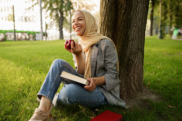 Arab girl in hijab holds apple and textbook