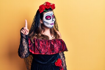 Young woman wearing day of the dead costume over yellow pointing finger up with successful idea. exited and happy. number one.