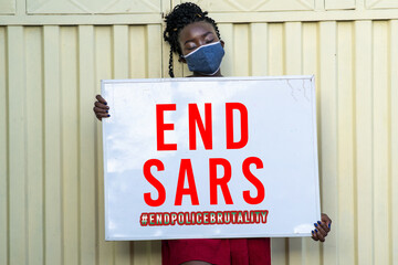 African female wearing a face mask and holding a sign with 'END SARS' written on it