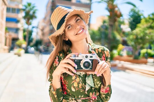 Beautiful caucasian woman smiling happy on a sunny day outdoors taking pictures using vintage camera