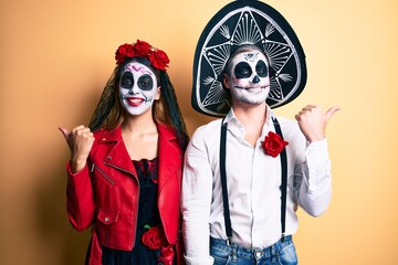 Plakat Couple wearing day of the dead costume over yellow smiling with happy face looking and pointing to the side with thumb up.