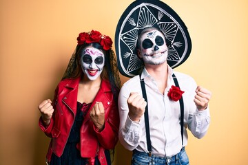 Couple wearing day of the dead costume over yellow very happy and excited doing winner gesture with arms raised, smiling and screaming for success. celebration concept.