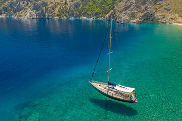 Aerial drone photo of sail boat docked in tropical mediterranean bay with crystal clear water
